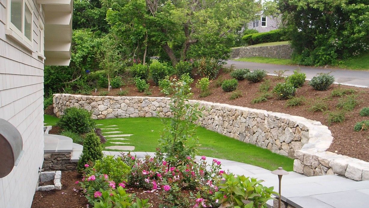 A red mini excavator works on a small construction project near a brick building on a sunny day.