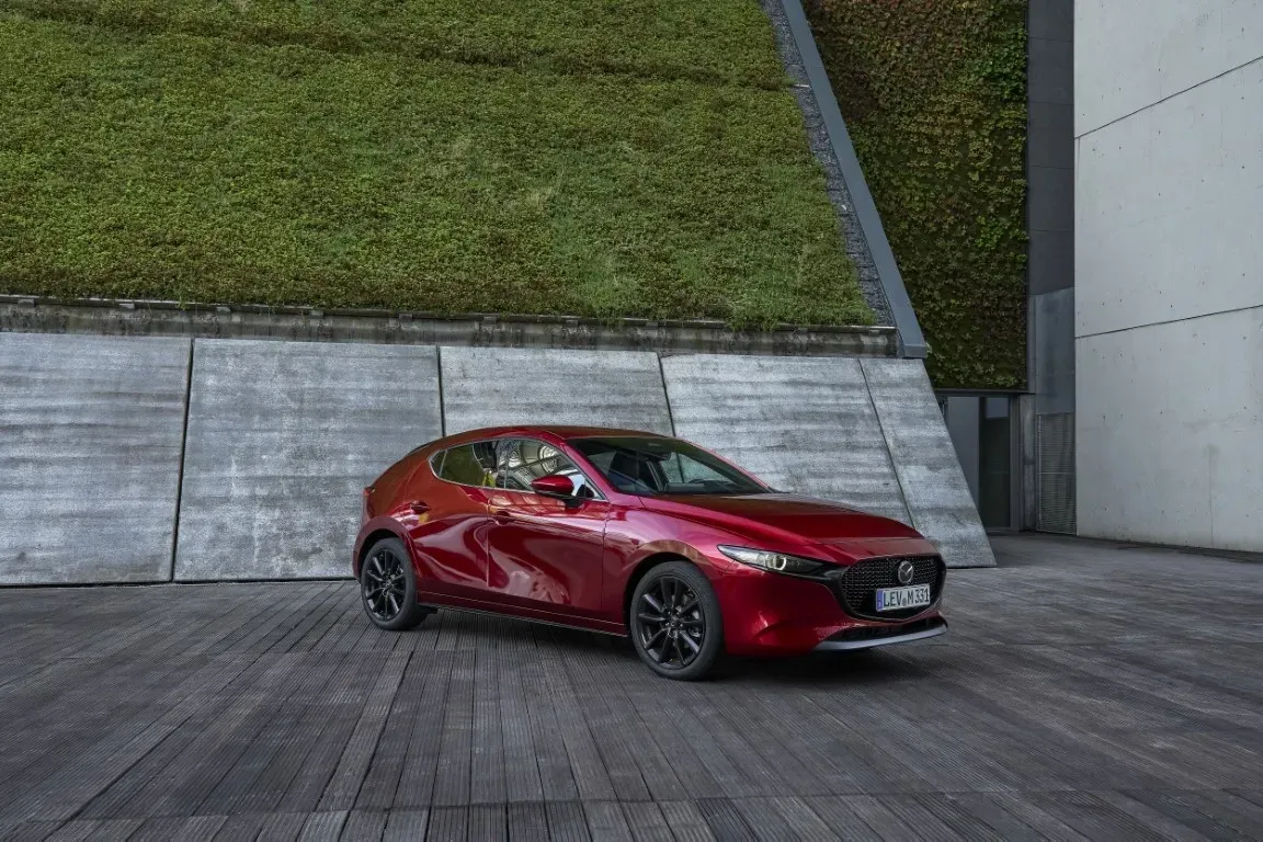 Ein roter Mazda-Kompaktwagen parkte auf einer Holzterrasse vor einer Betonmauer mit einem großen, grünen vertikalen Garten.