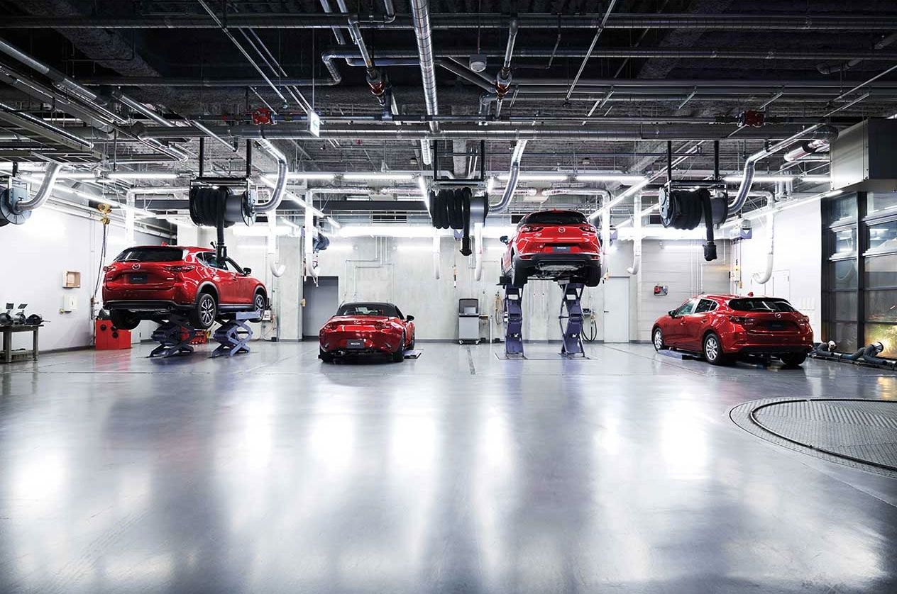 Eine hell erleuchtete Autowerkstatt mit vier roten Mazda Modellen