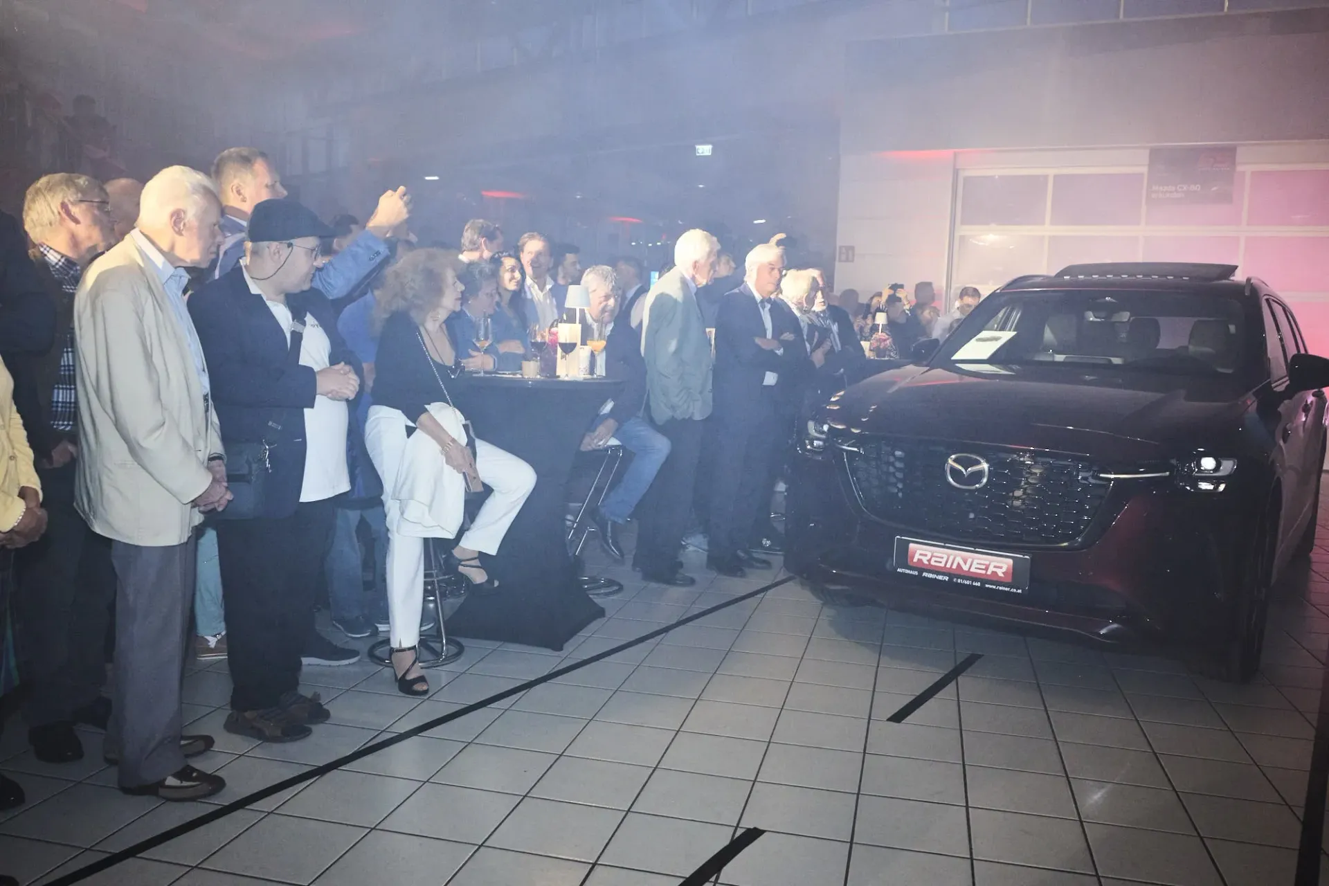 In einer Halle steht eine Menschenmenge um einen dunklen Geländewagen