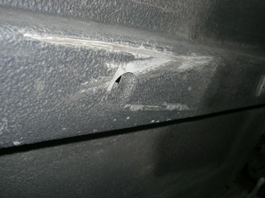 Nahaufnahme einer dunklen, strukturierten Oberfläche mit einer kleinen Einstichstelle und umgebenden Kratzern.