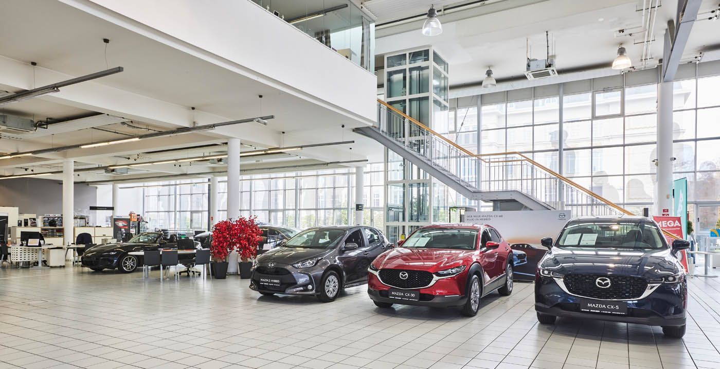 Moderner Ausstellungsraum eines Autohauses mit mehreren geparkten Mazda-Fahrzeugen, darunter rote und dunkelgraue SUVs.