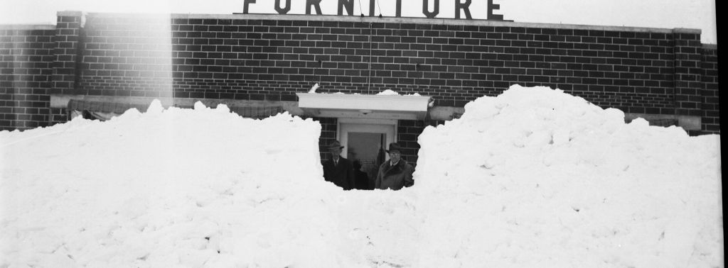 A black and white photo of a furniture store covered in snow.