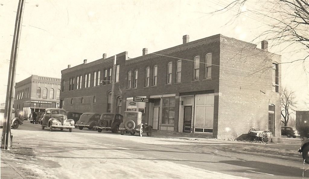 A black and white photo of a brick building with cars parked in front of it