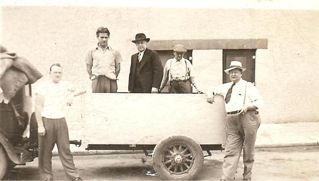 A group of men are standing in front of an old car