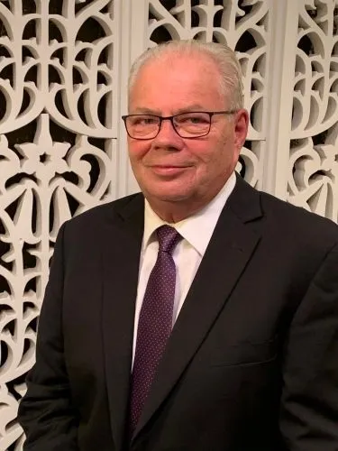 A man is wearing a black columbia vest and smiling.