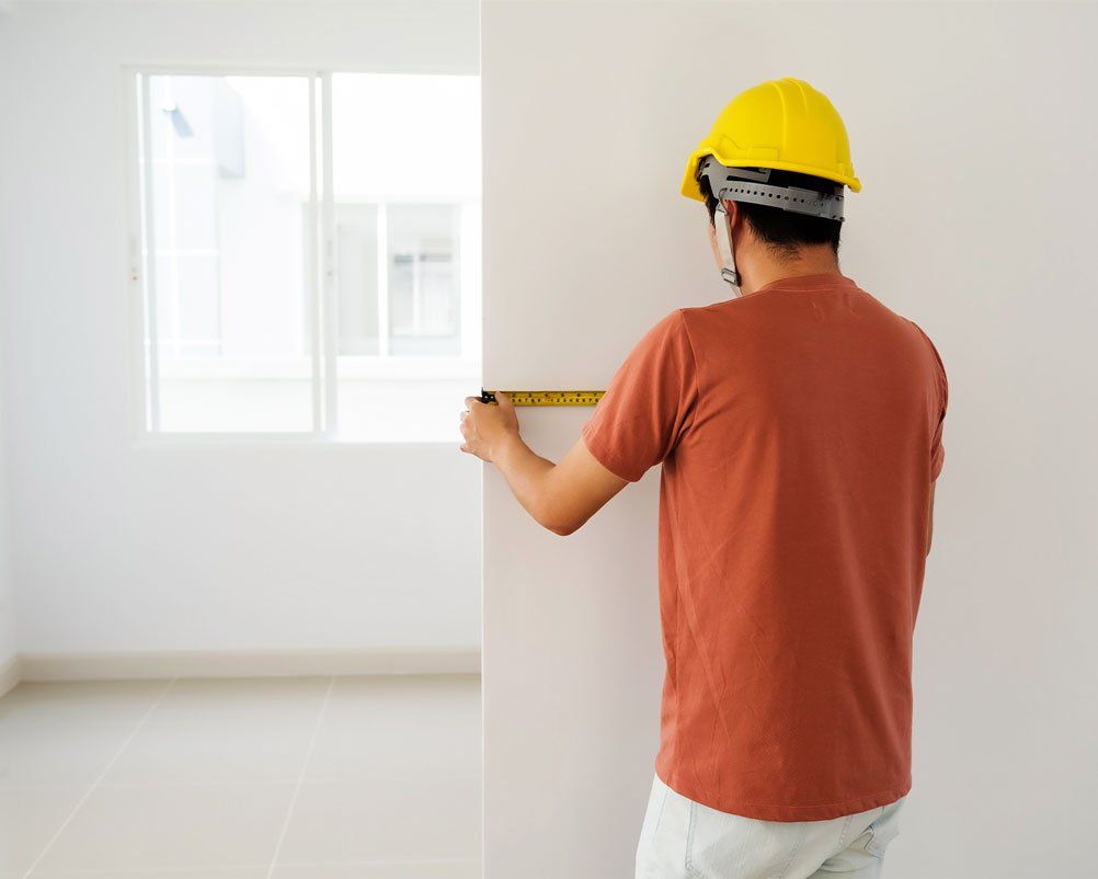 Builder in yellow hard hat measuring a white wall