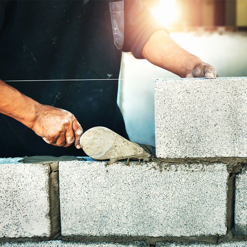 man with a trowel laying mortar to build a grey stone wall