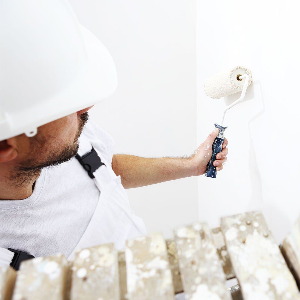 man in white helmet painting white wall with a roller