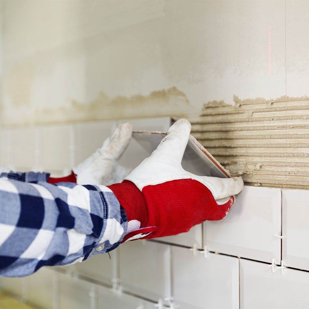 man with red gloves fixing a wall tile