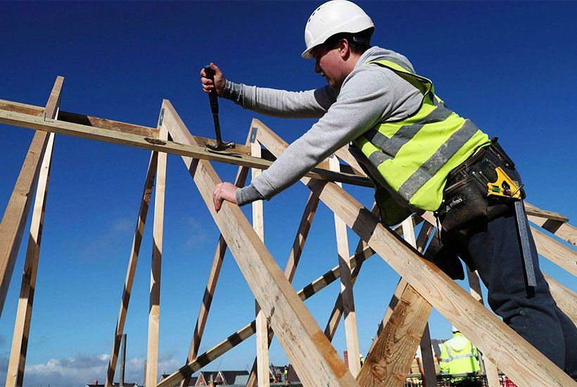 Builder in a white helmet removing a nail from a plank of wood with a hammer