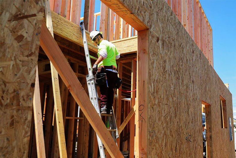 Builder in white helmet standing on a ladder building wooden house foundations