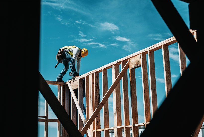 Builder in yellow helmet building wooden house foundations