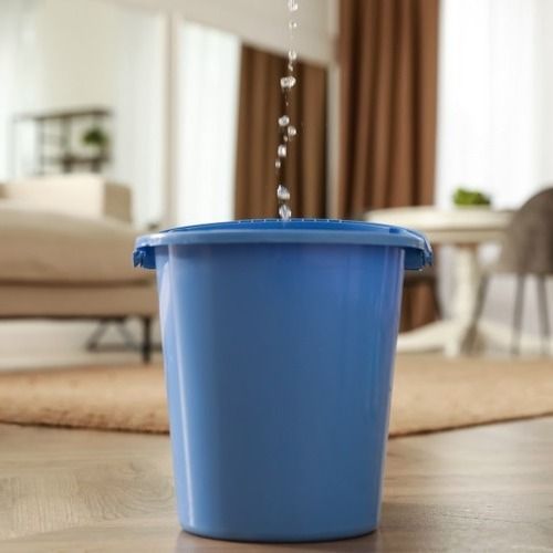 Blue bucket containing raindrops from leaking roof