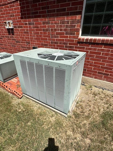 A white air conditioner is sitting in front of a brick building.