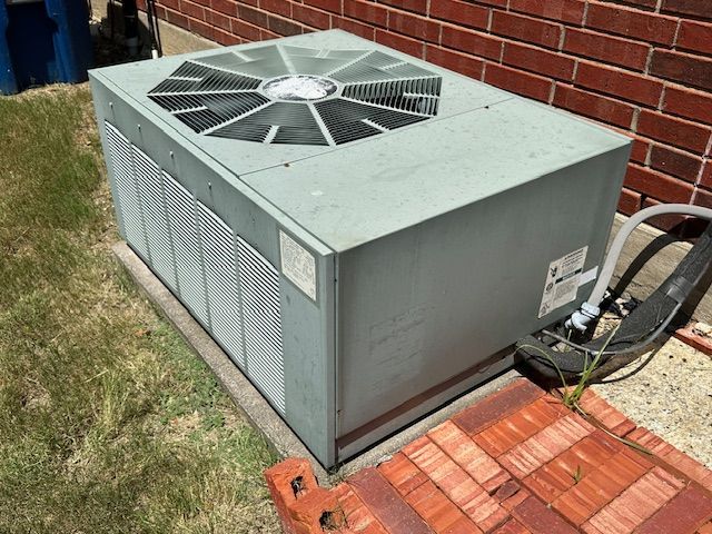 An air conditioner is sitting on the side of a brick building.