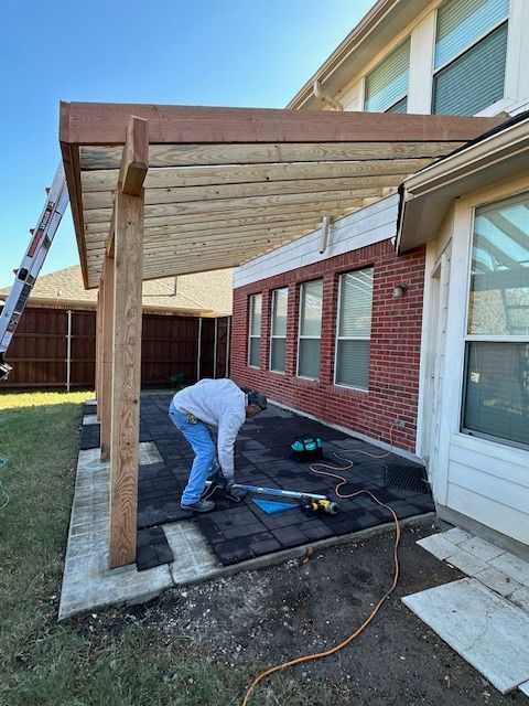 A man is working on a pergola in front of a brick house.