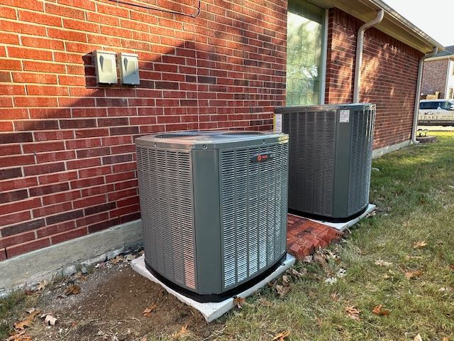 Two air conditioners are sitting on the side of a brick building.