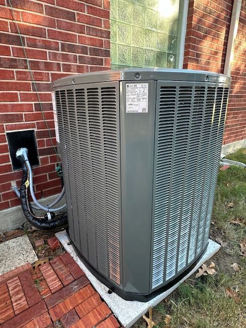 A large air conditioner is sitting outside of a brick building.