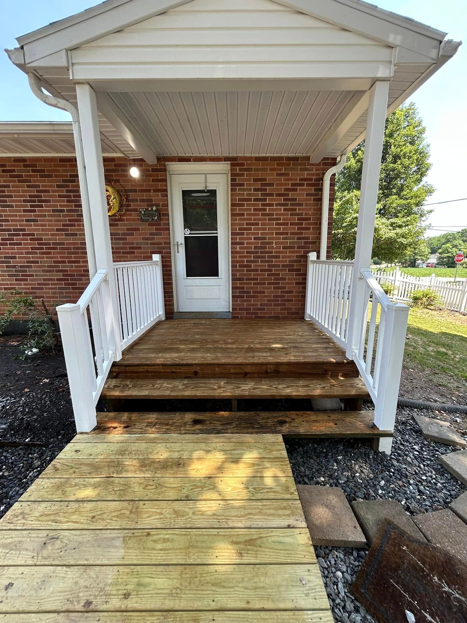 The front porch of a brick house with a wooden walkway leading to it.