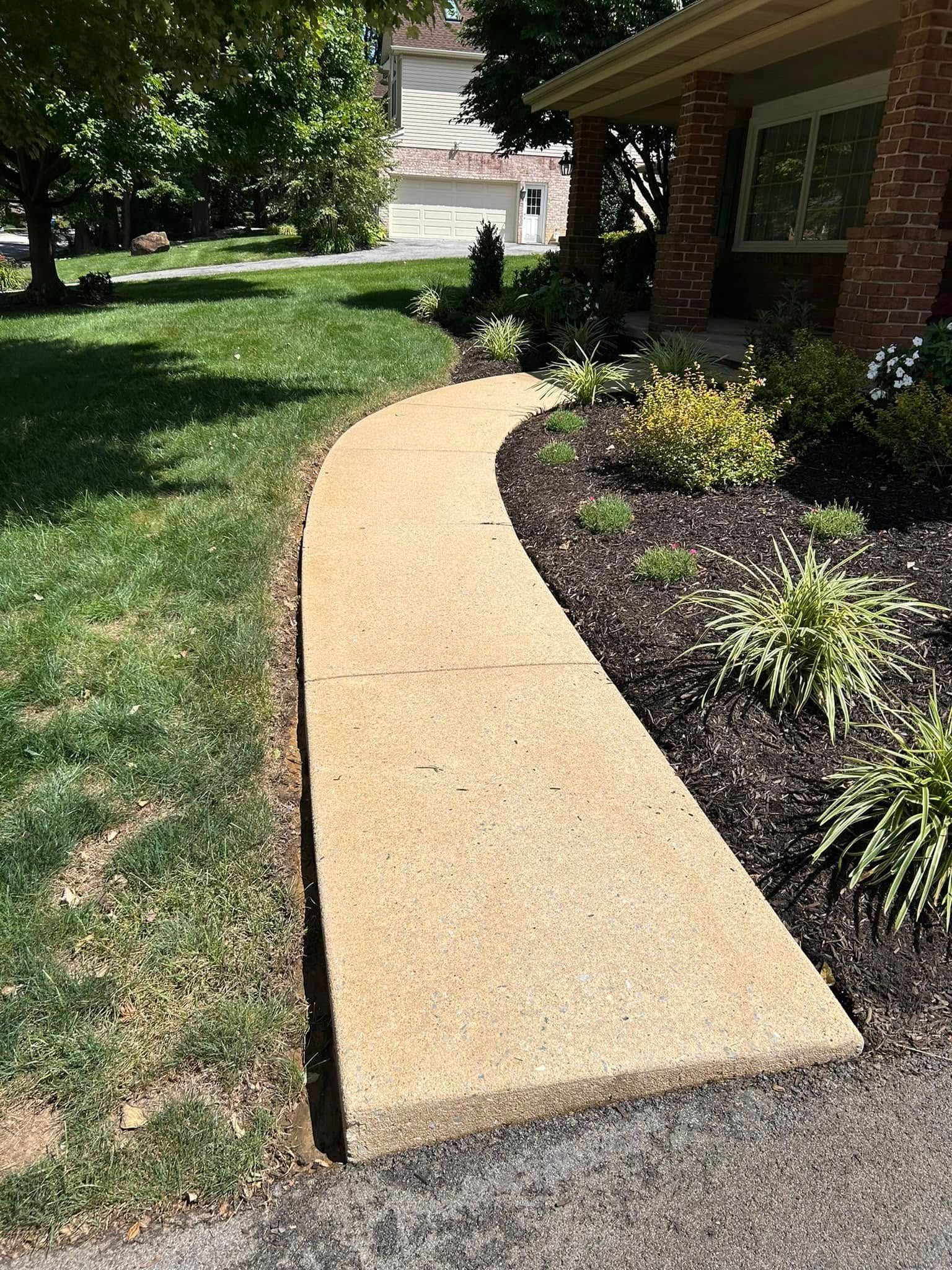 A concrete walkway leading to a house with a brick house in the background.