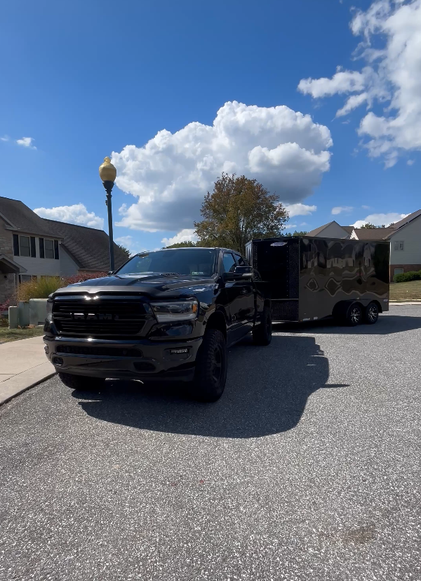 Black truck with trailer parked on pavement under a partly cloudy sky.