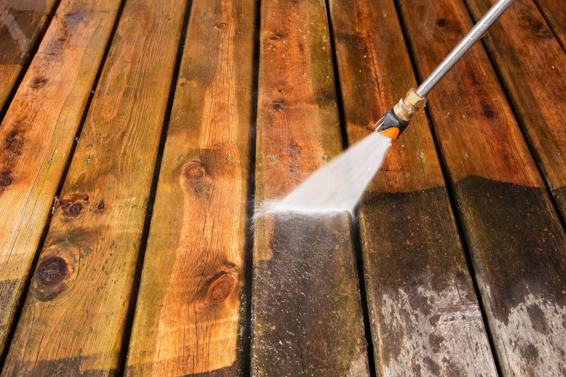 A person is cleaning a wooden deck with a high pressure washer.