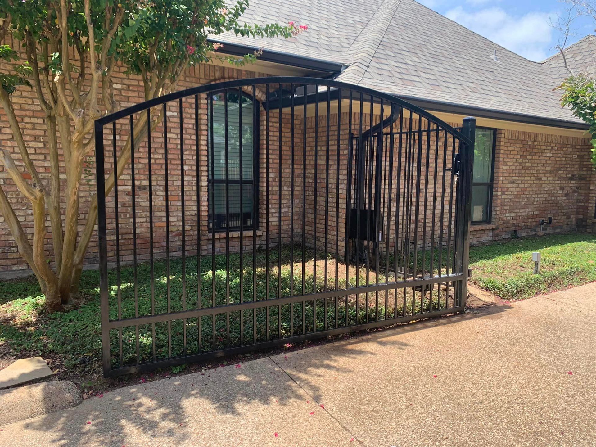 Black wrought-iron gate in front of a brick house with a green lawn.