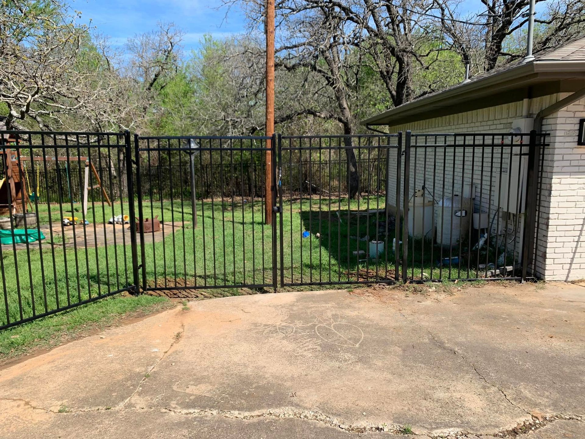 Black metal fence encloses a grassy yard next to a brick building.
