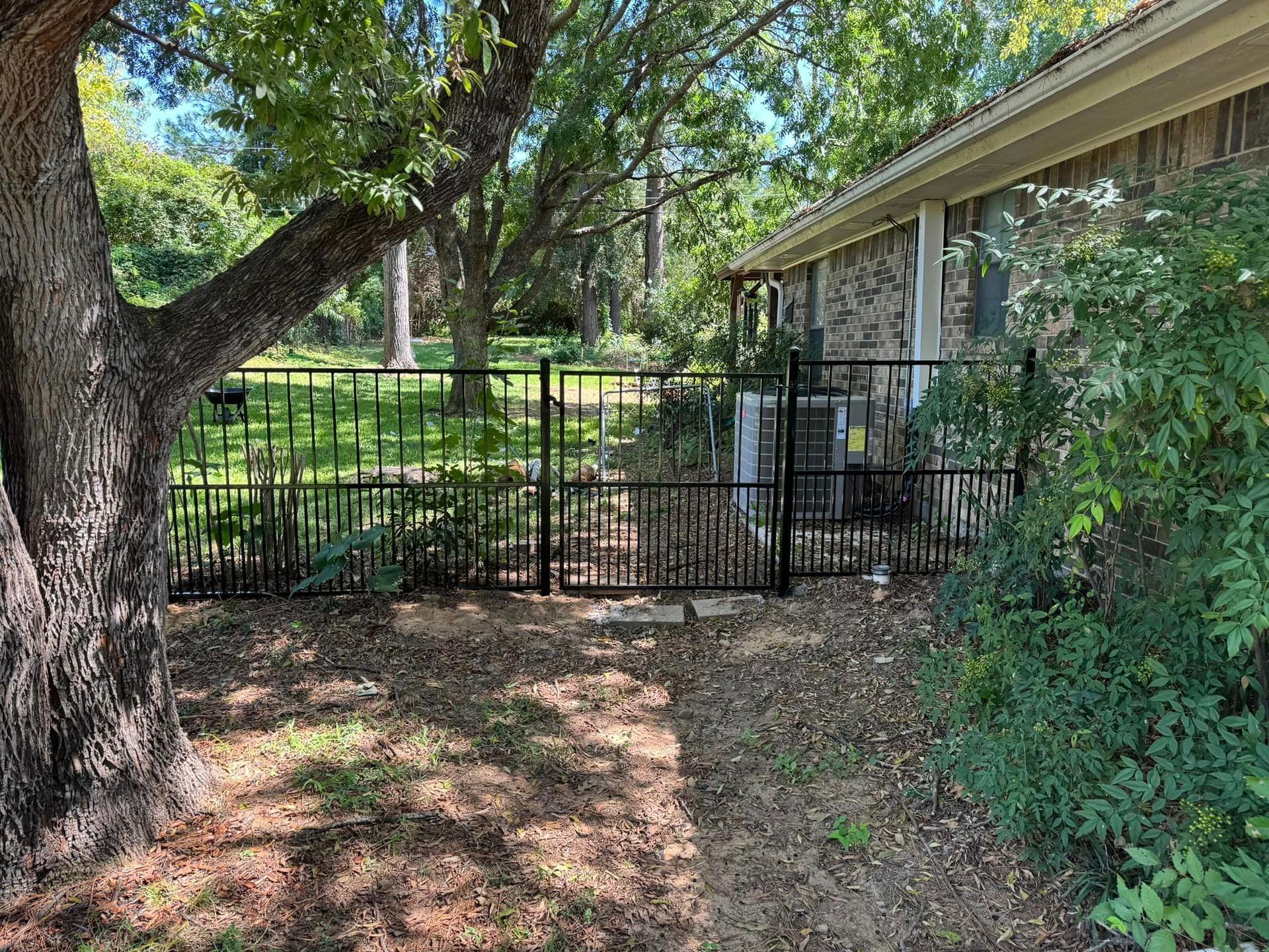 Black fence surrounding a yard with tree, building, and air conditioning unit.