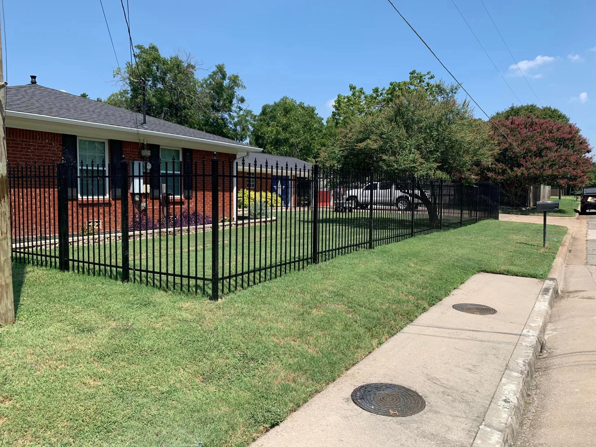 Black metal fence along a residential yard with grass and sidewalk.