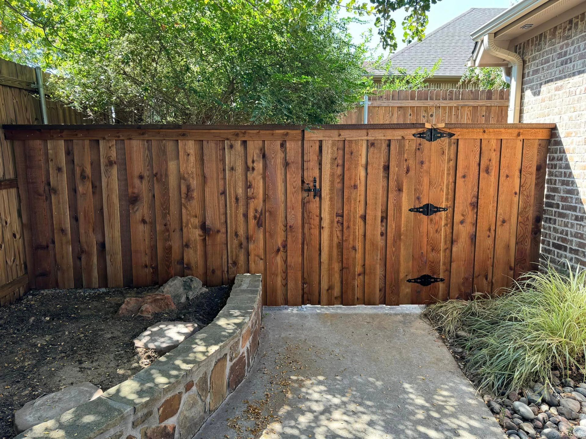 Wooden gate with black hardware set in a brown fence.