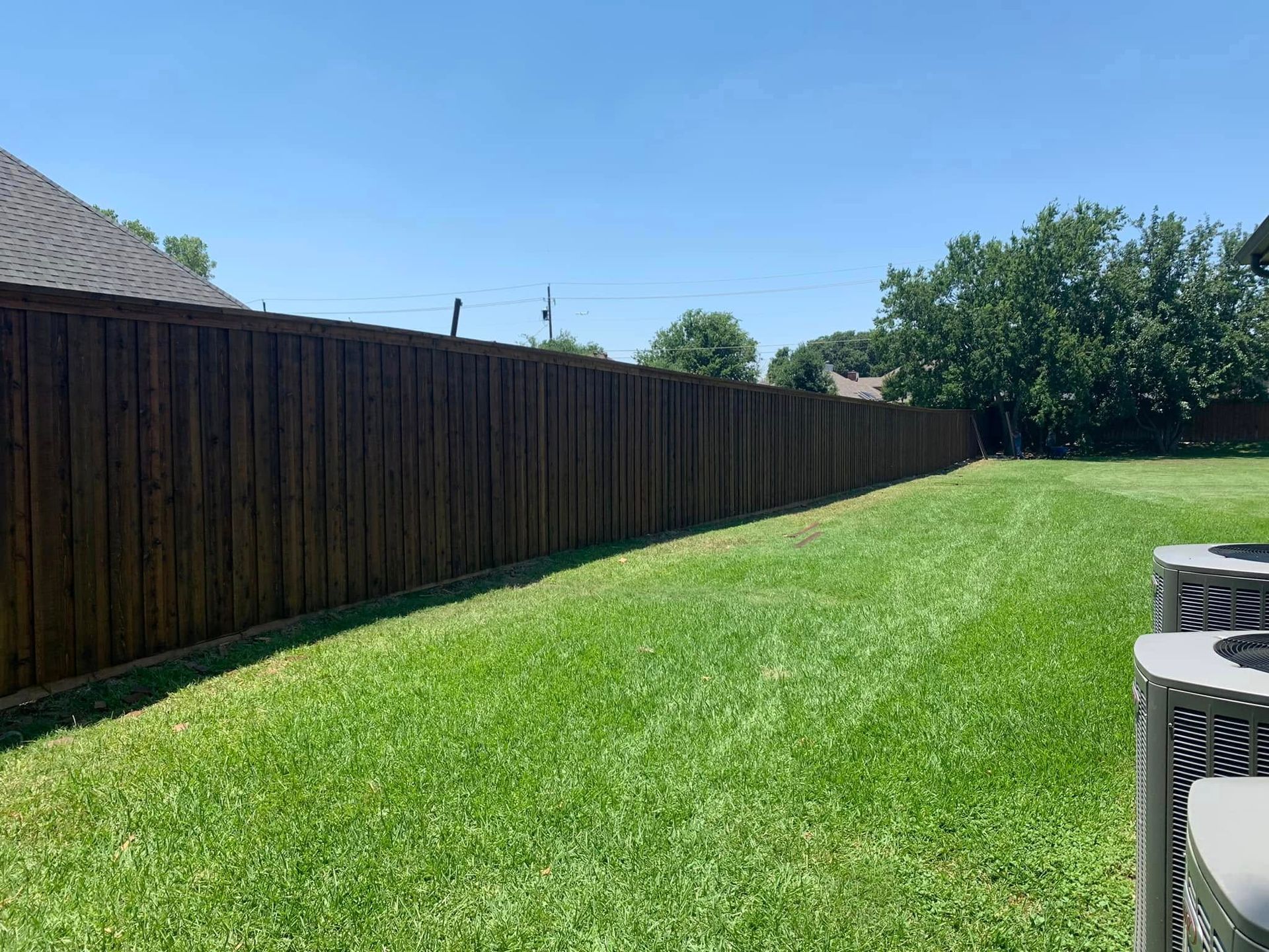 Dark brown wooden fence along a green lawn under a clear blue sky.