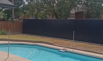 A backyard with a swimming pool, a black metal fence, and a grassy lawn.