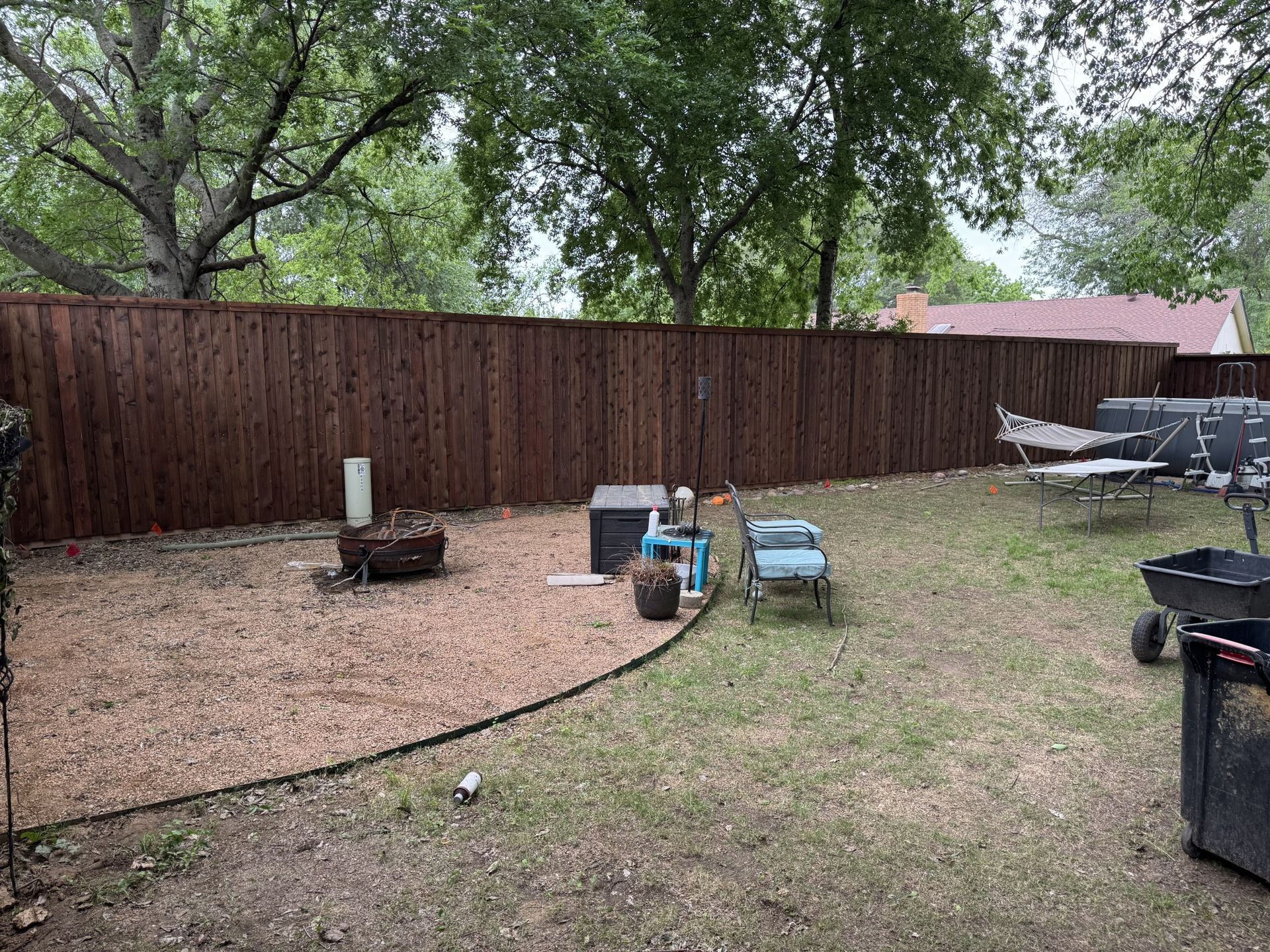 Backyard with brown fence, fire pit, gravel area, and various yard items.