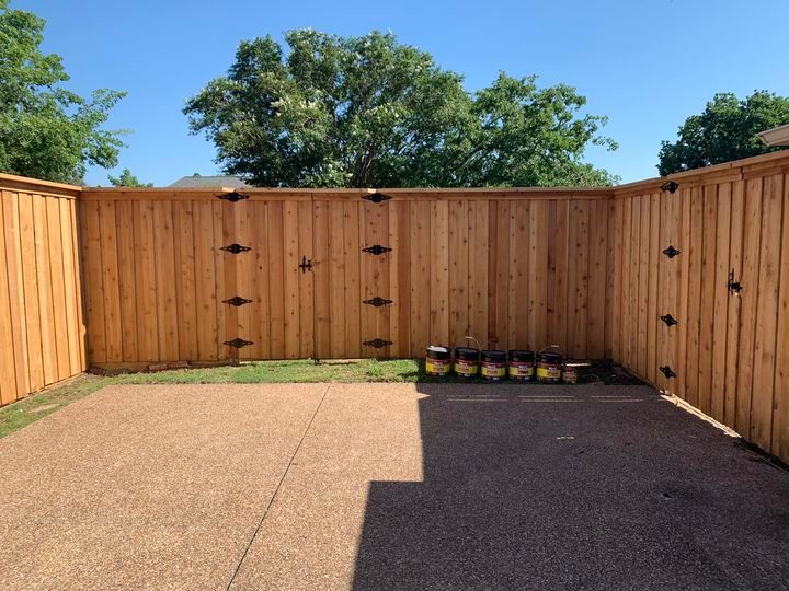 Wooden fence encloses a gravel patio and patch of grass on a sunny day.