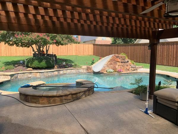 Backyard pool with a slide, surrounded by grass, and a wooden pergola overhead.