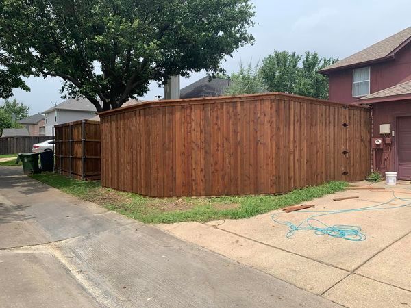 Brown wooden fence bordering a property corner, next to a driveway and a house.