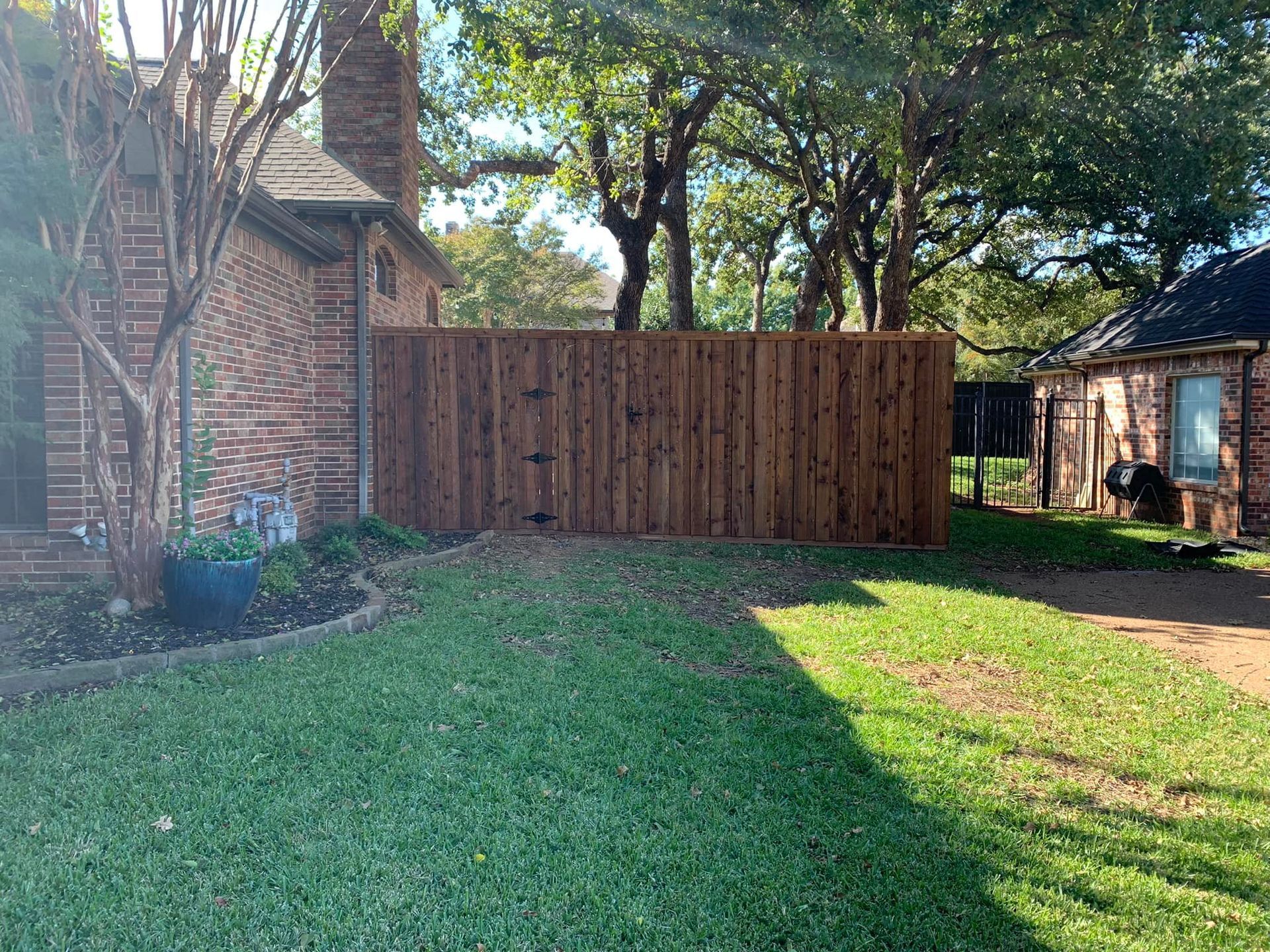 Lawn with a brown wooden fence separating two brick houses under a sunny sky.