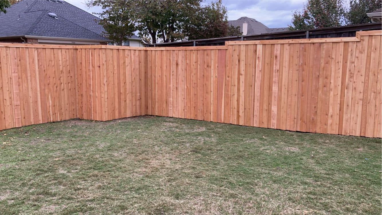Brown wooden fence in a grassy backyard, under a cloudy sky.