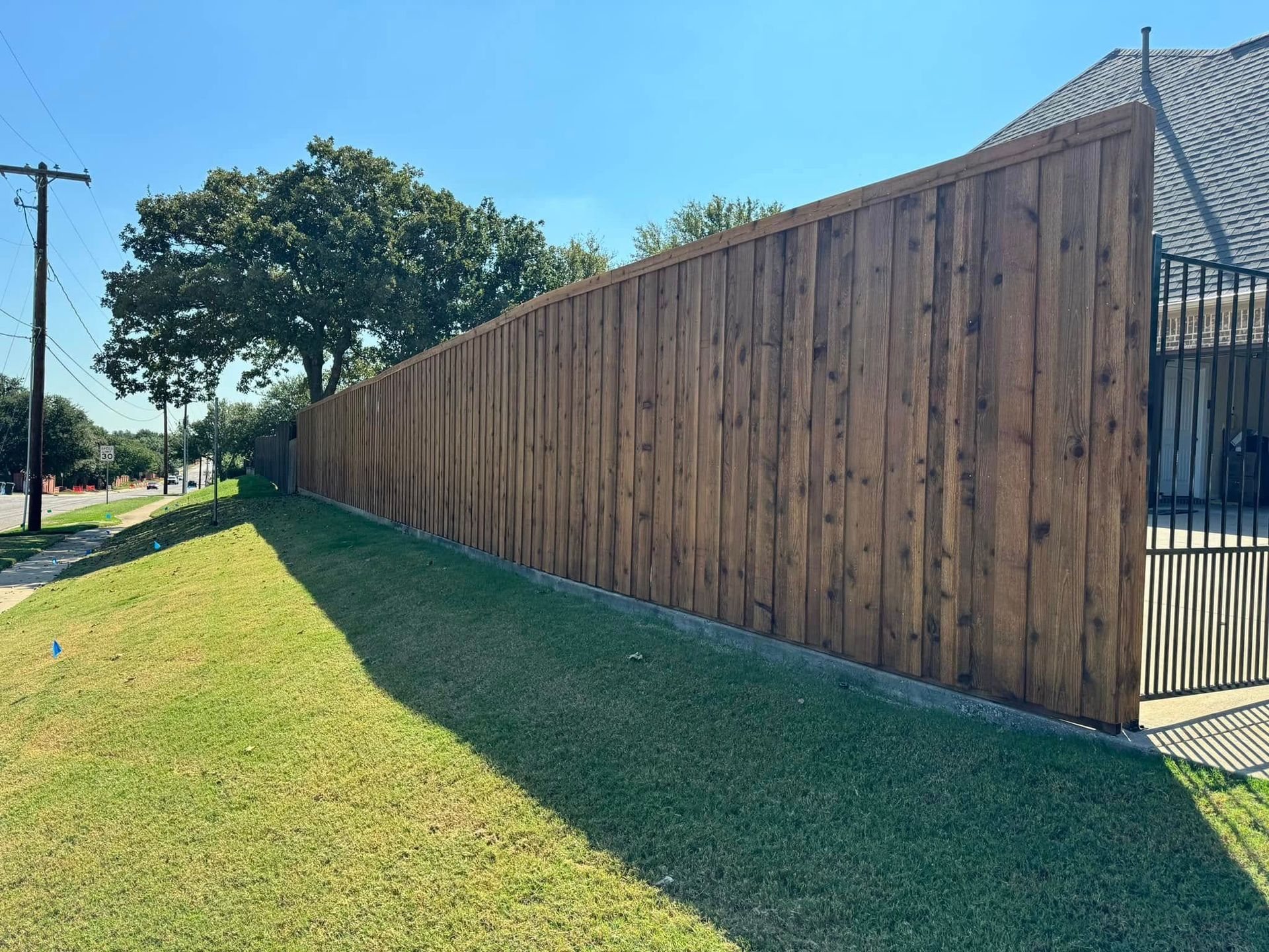 Wooden fence along a grassy lawn with a clear blue sky overhead.