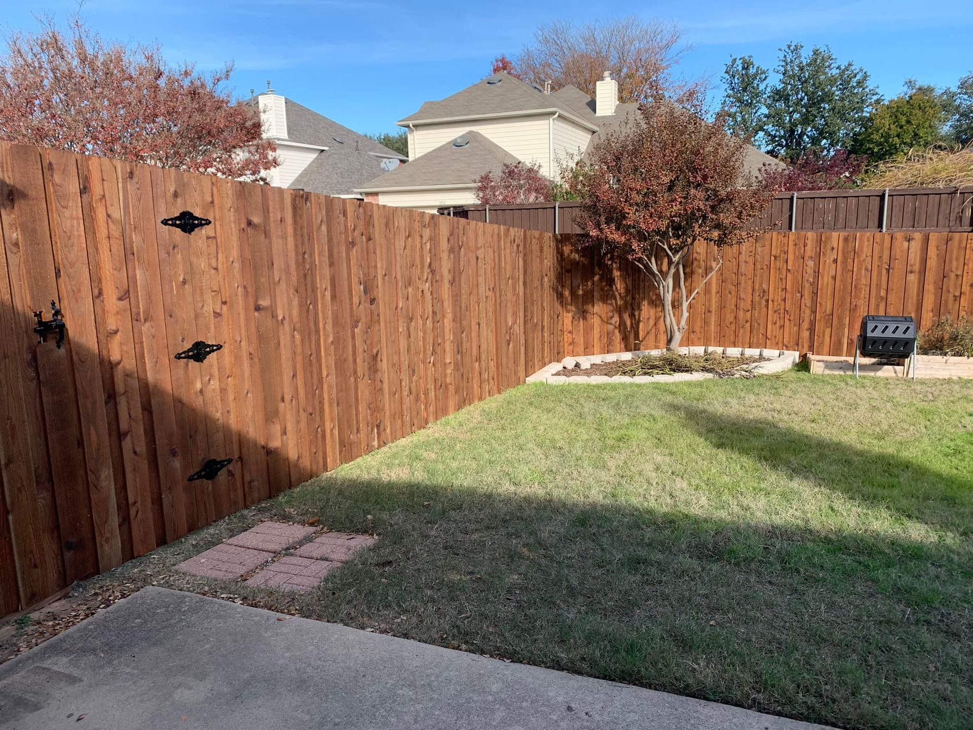 Wooden fence surrounding a small backyard with grass, small tree, and blue sky.