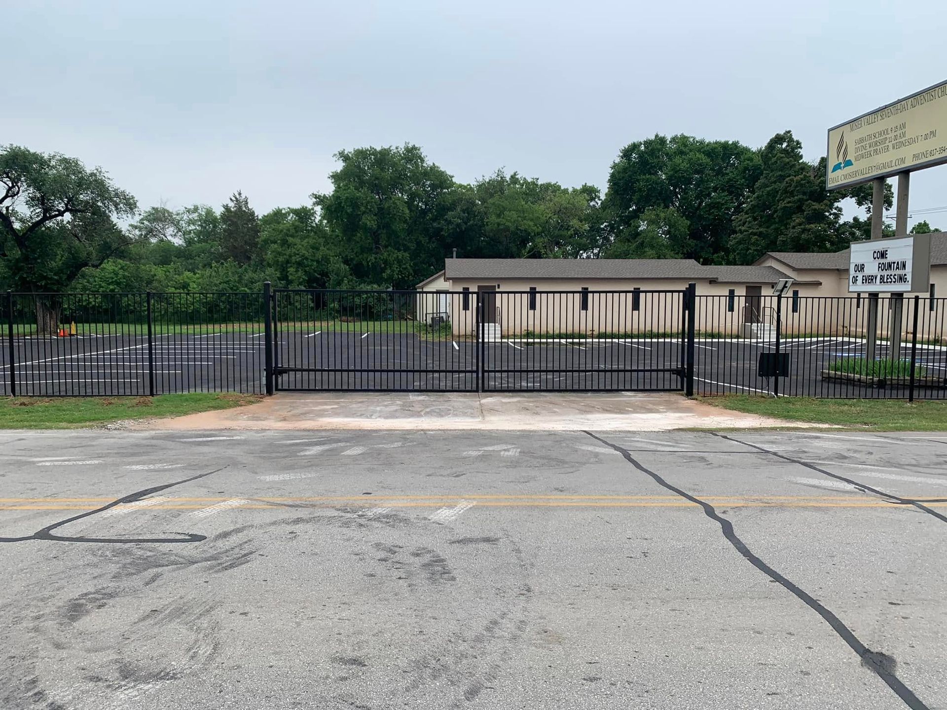 Black gate at entrance of building with sign; overcast sky, asphalt road.