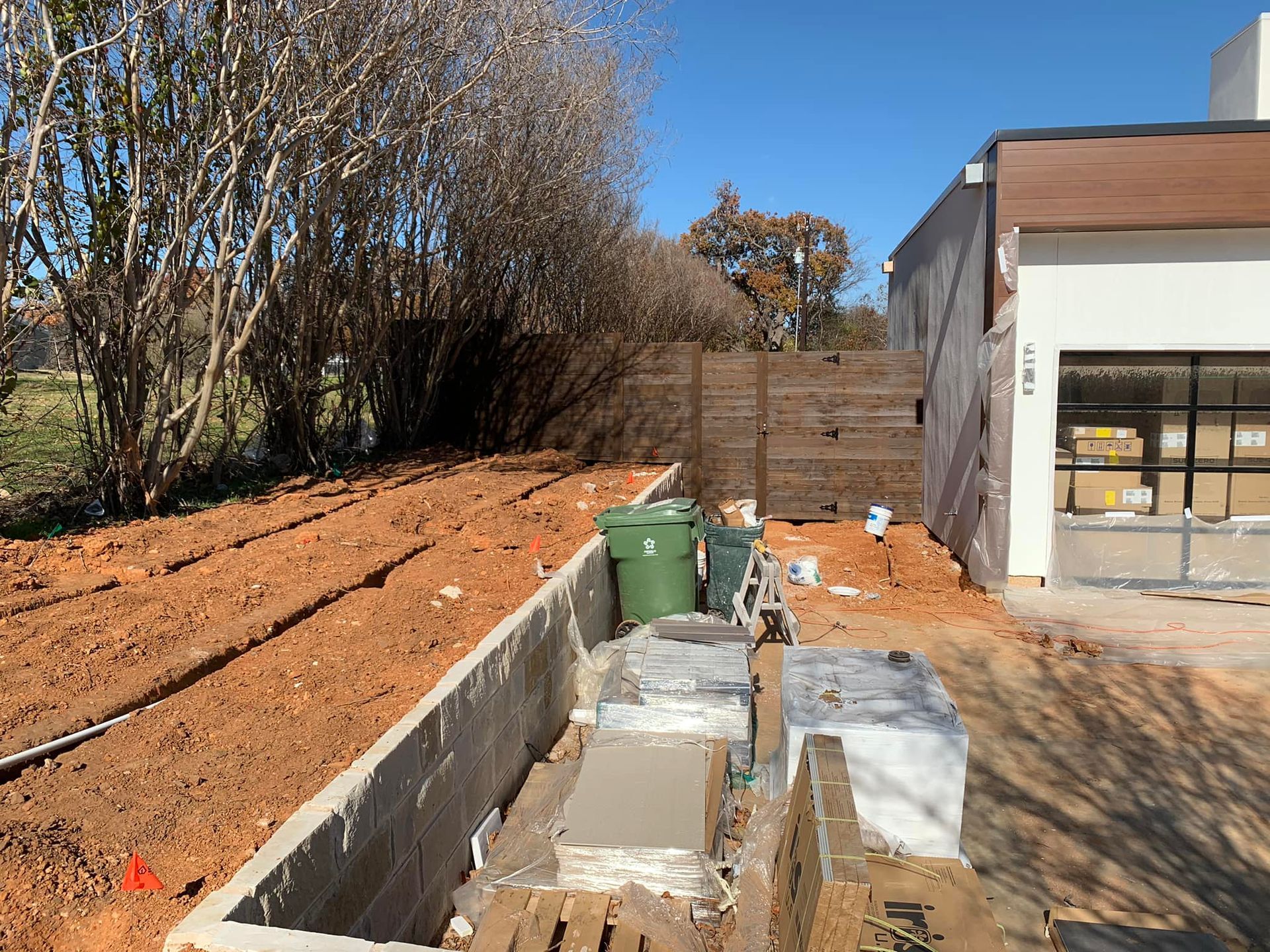 Construction site with a retaining wall, dirt, and green trash cans.