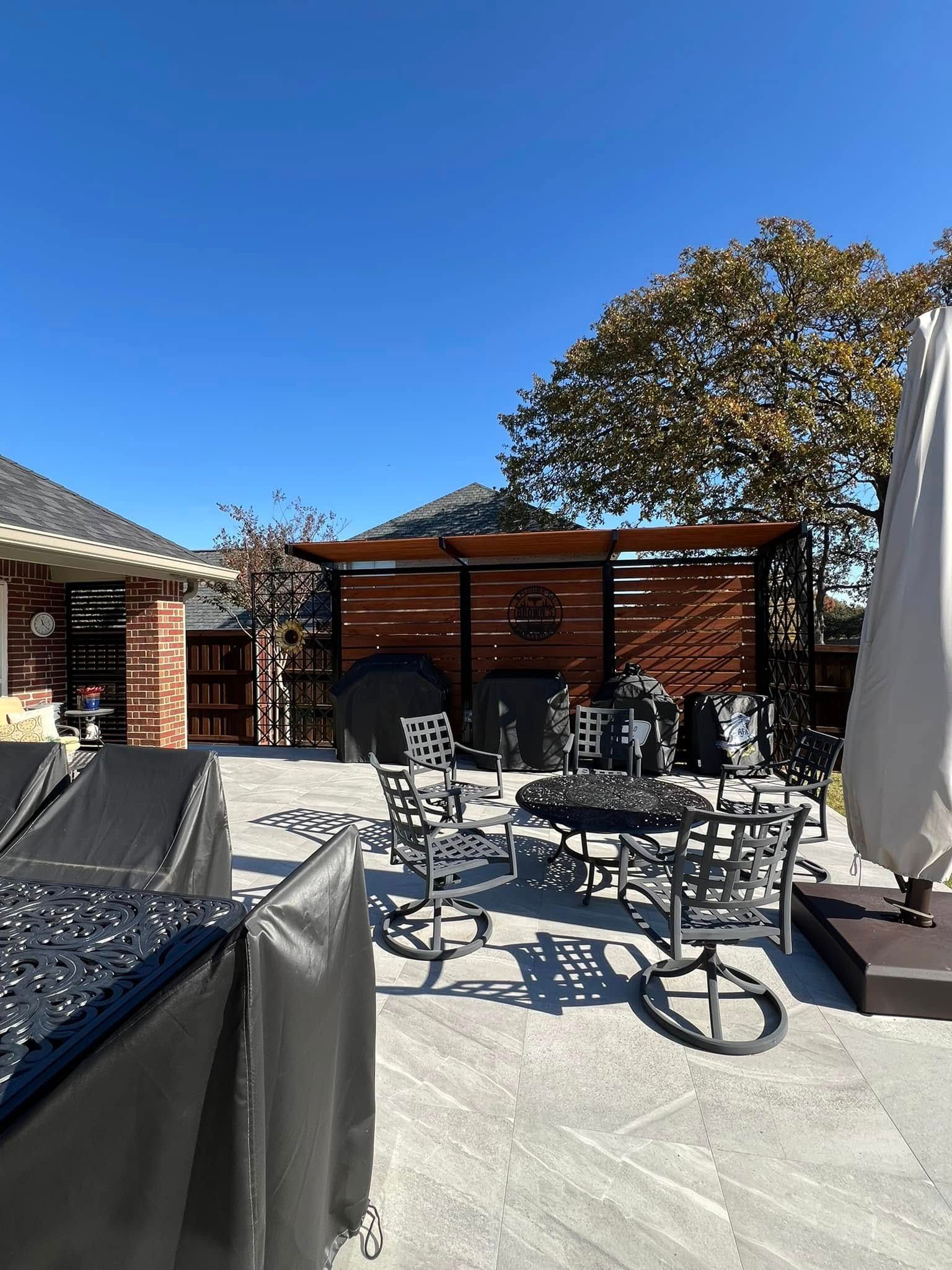 Outdoor patio with metal furniture, grill area with wooden pergola, clear blue sky.