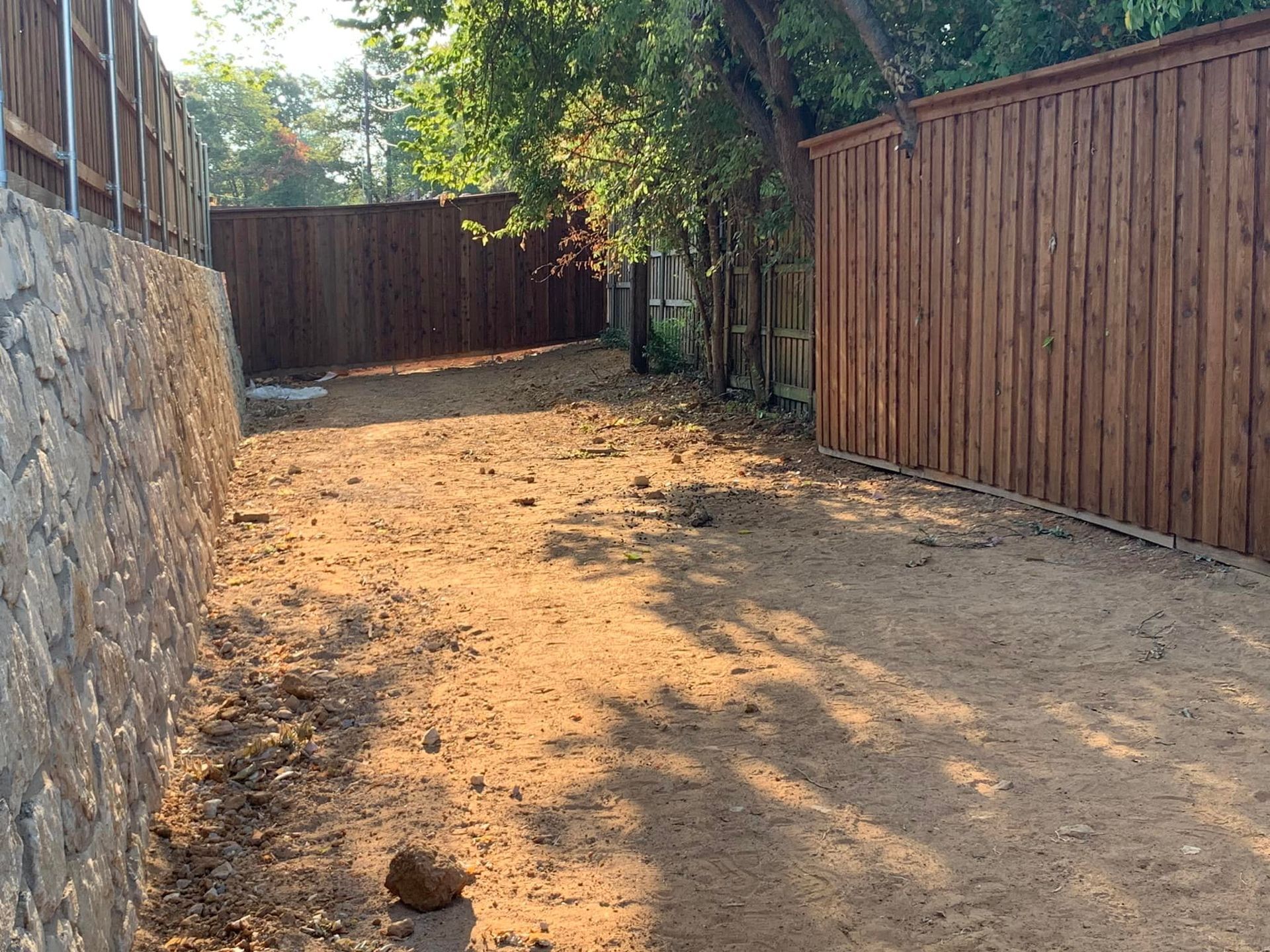 A sandy, dirt yard bordered by wood fences and a stone retaining wall.