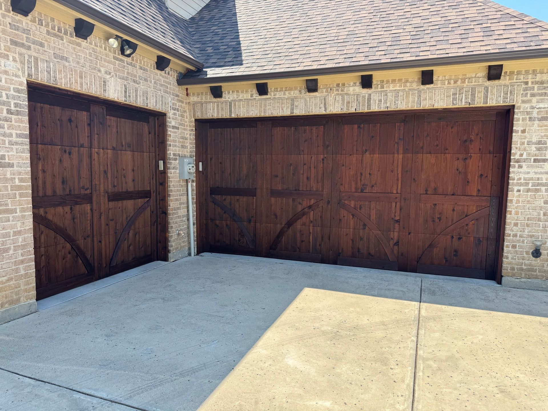 Two brown wooden garage doors on a brick house. Concrete driveway.