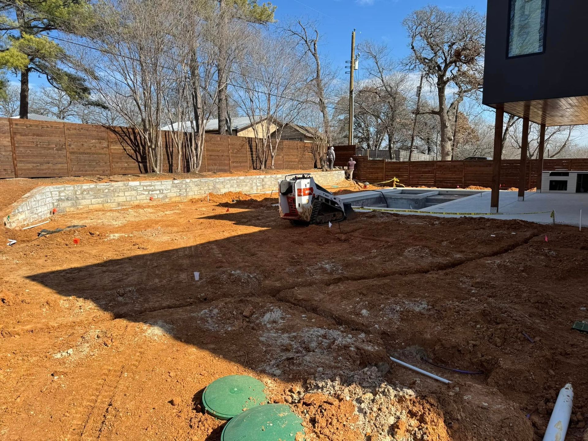 Construction site with a small excavator, trenches, and a retaining wall.