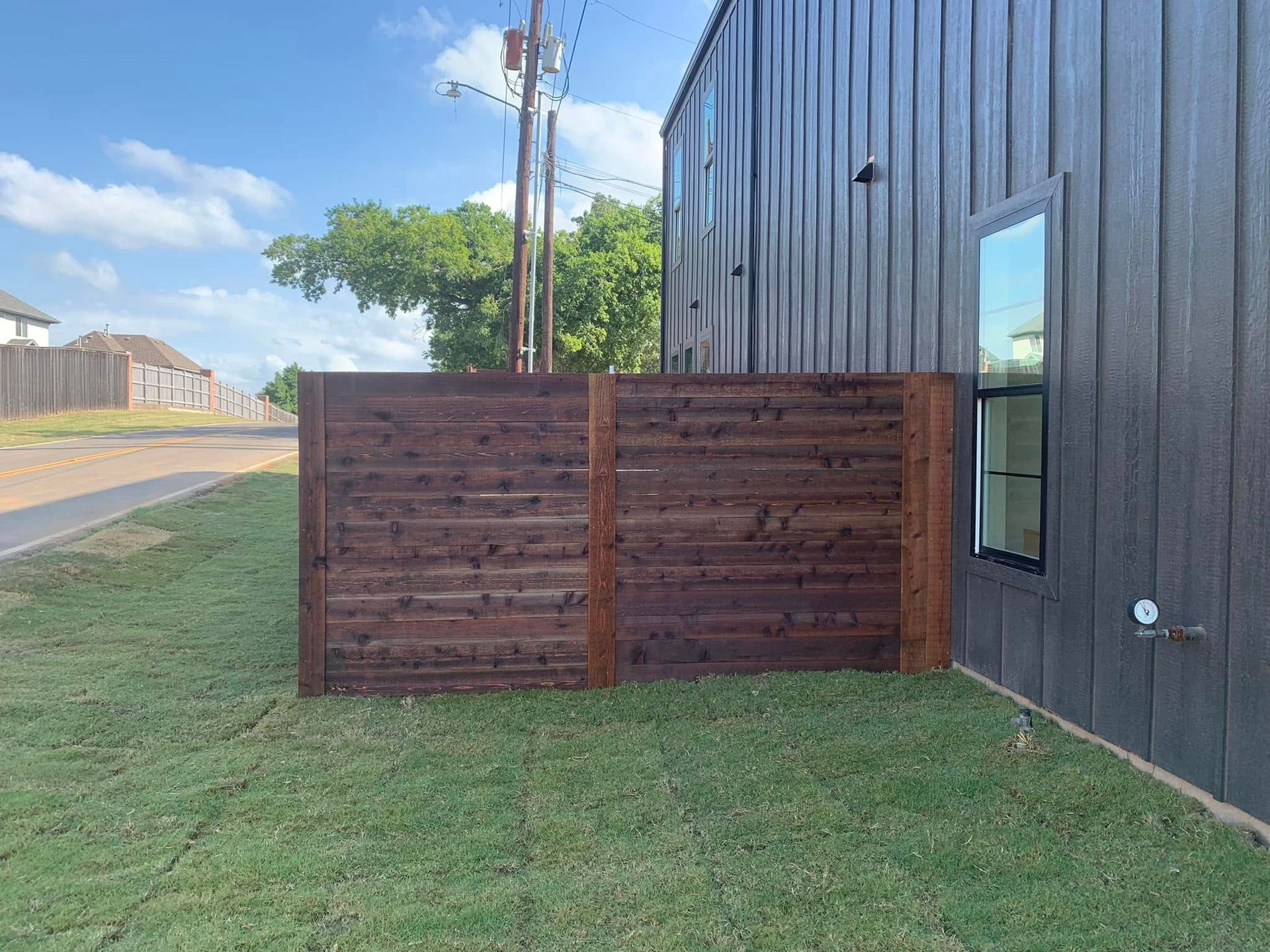 Dark brown horizontal slat fence in a grassy yard beside a dark gray house.
