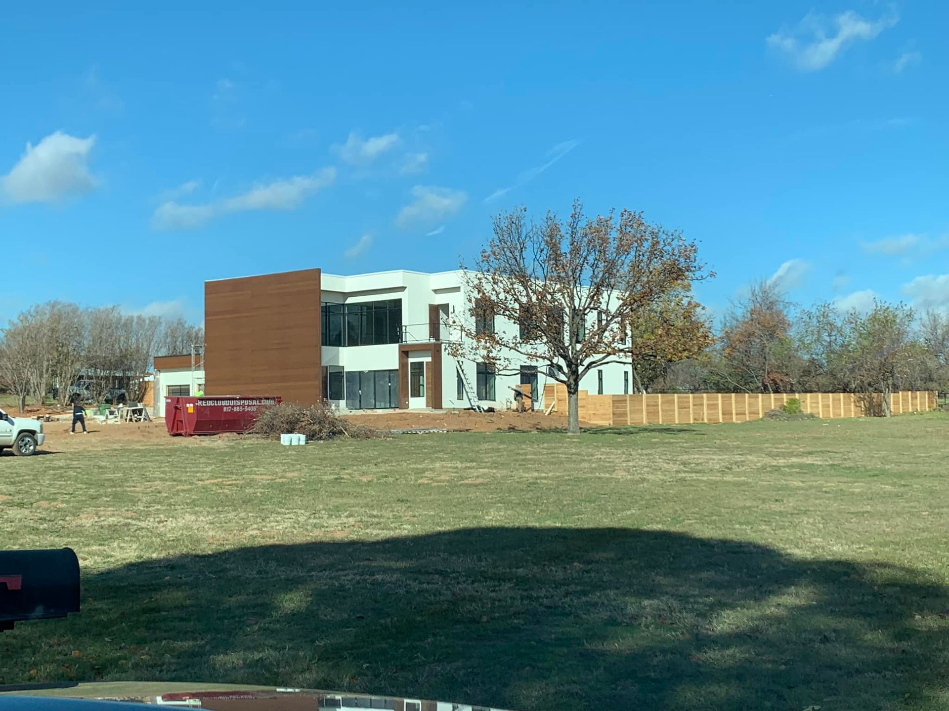 Modern two-story house with brown siding and white walls under a blue sky on a grassy lot. Construction workers present.